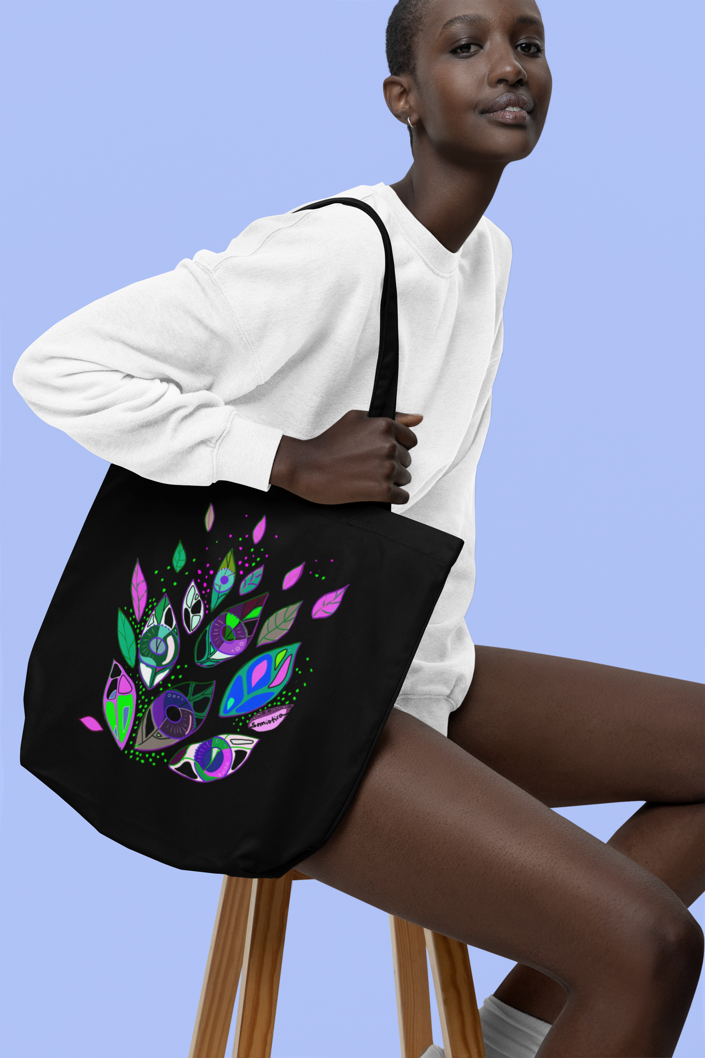 Model sitting with black Semiòtica tote bag over shoulder, showing symbolic Seeds of Seeing print.